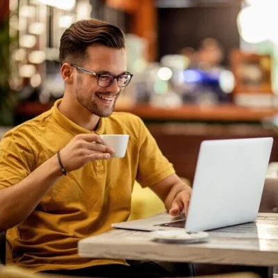 young-smiling-man-typing-computer-while-browsing-internet-drinking-coffee-bar_637285-2064-e1703342475918